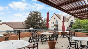 An outdoor patio area with round tables and chairs, red umbrellas, and a pergola.