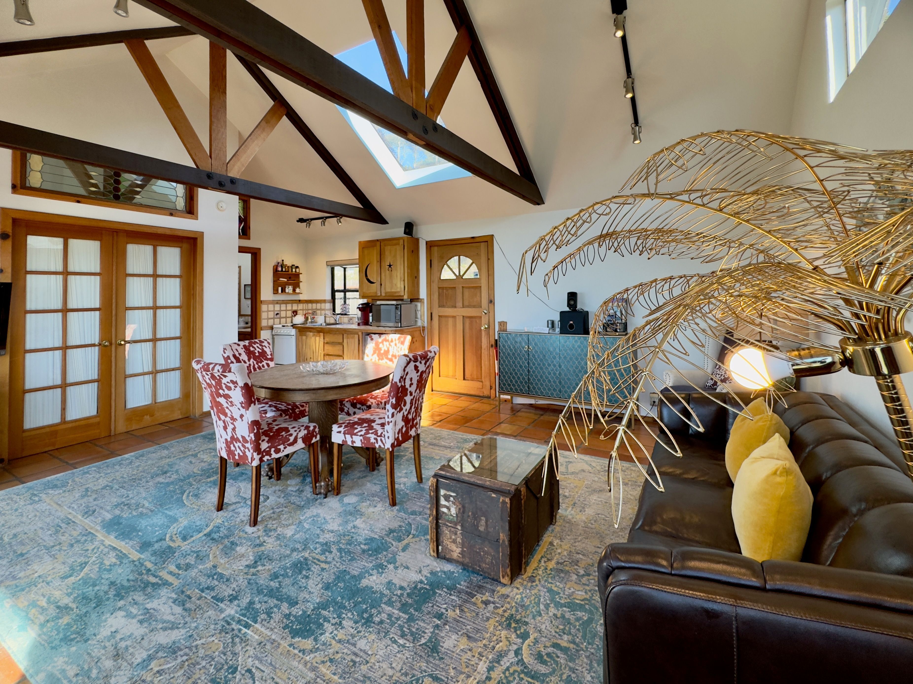 Un salon spacieux avec un plafond haut, un coin repas avec des chaises à motifs, un canapé avec des coussins et une lampe décorative.