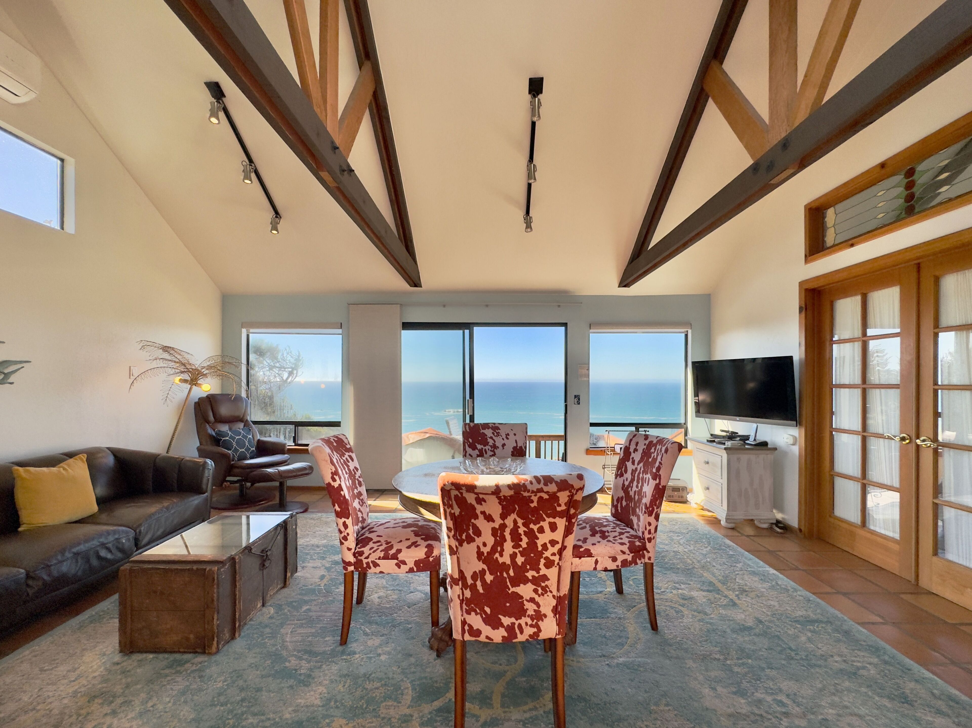 Un vaste salon doté d’une grande fenêtre donnant sur la mer, un coin salon confortable avec un canapé et des fauteuils, et une table à manger avec vue.