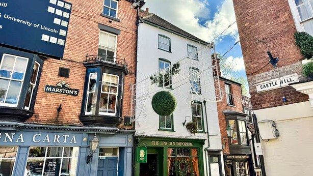 Une vue de rue avec des bâtiments portant les noms « Marston’s », « The Lincoln Imporium » et « Castle Hill ».