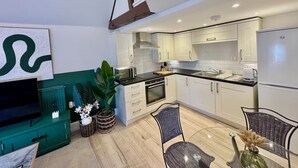 Une cuisine moderne avec des armoires blanches, un comptoir noir et un réfrigérateur en acier inoxydable. On y trouve un coin repas avec des chaises en osier et une table en verre.