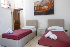 Habitación de hotel con dos camas, una mesita de noche, una puerta y un cuadro de paisaje urbano en la pared.