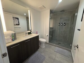 Ein modernes Badezimmer mit einer gläsernen Dusche, einem großen Spiegel und einem dunklen Waschtisch.