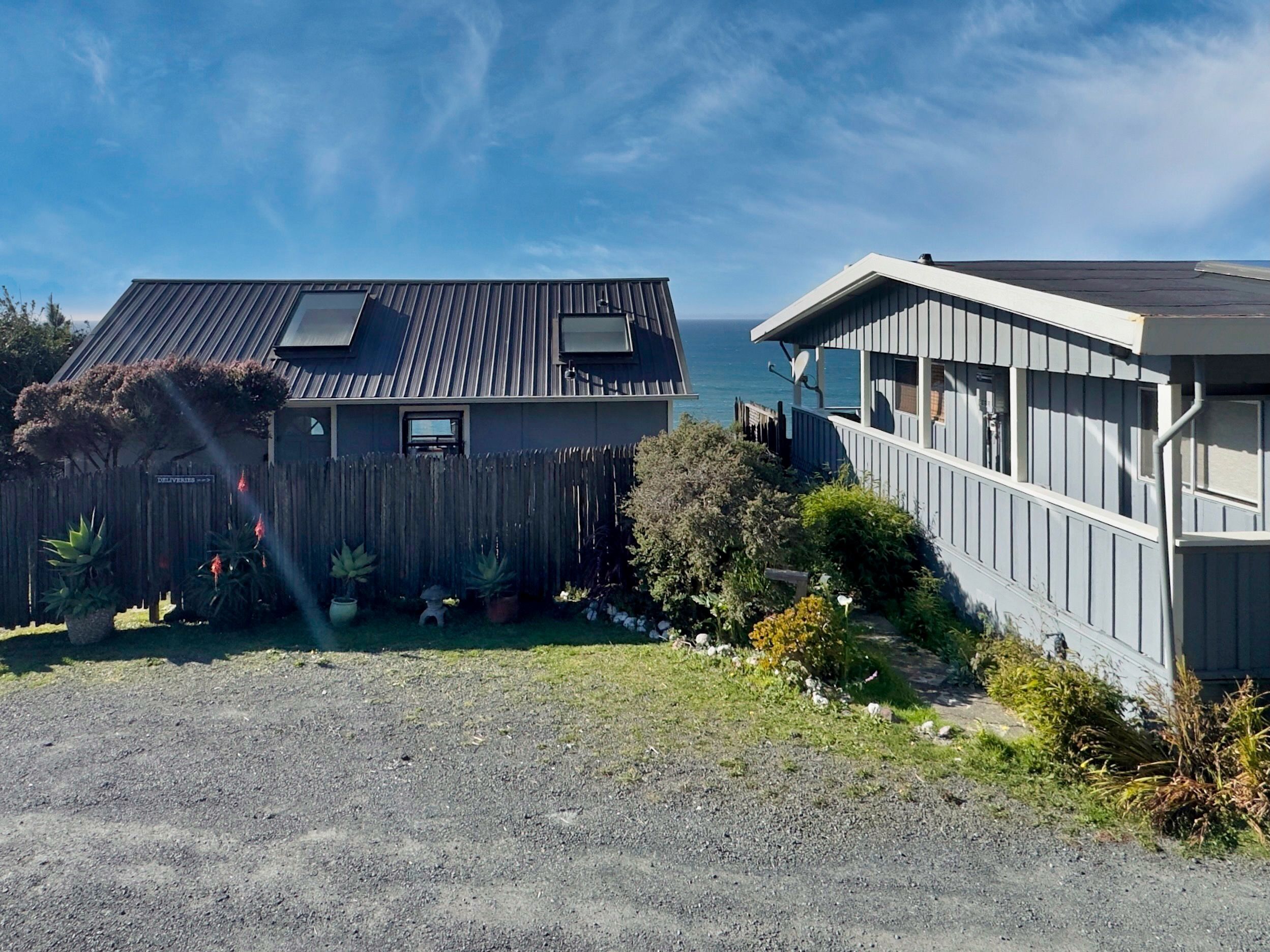 A residential property with two houses, one with a sloped roof and another with a flat roof, both featuring large windows and a gravel driveway.