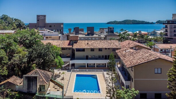 Un hôtel situé sur la côte, doté d’une piscine, de bâtiments aux toits de tuiles rouges et offrant une vue sur la mer.