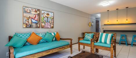 Una sala de estar con un sofá, dos sillas de madera, una mesa de centro y obras de arte en la pared.