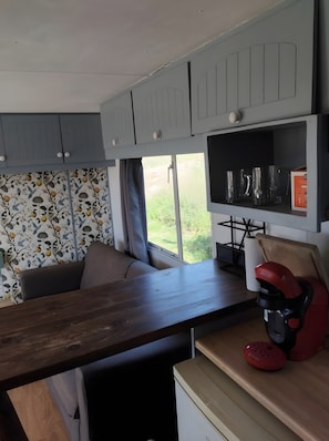 Une cuisine compacte avec un plan de travail en bois, une machine à café rouge et une fenêtre donnant sur un paysage verdoyant.