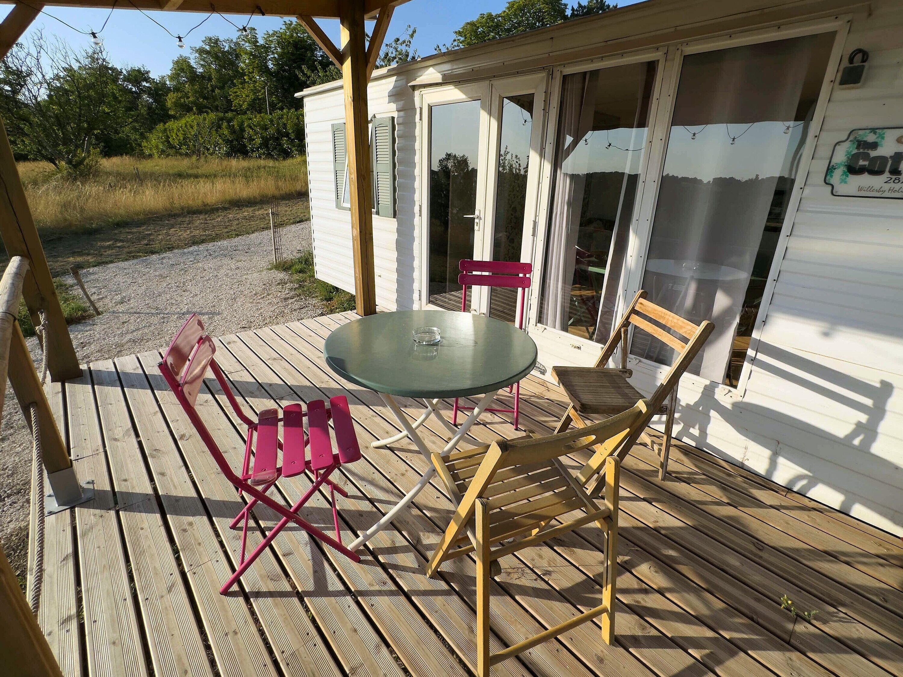 A wooden deck with a glass table and two chairs, a small wooden structure with a door, and a sign with text.
