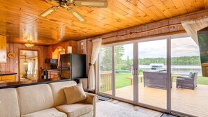 L’intérieur chaleureux d’un chalet avec un plafond en bois, un canapé, un téléviseur et une porte-fenêtre coulissante donnant sur une terrasse extérieure.