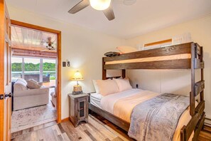 Une chambre avec un lit superposé, un ventilateur de plafond, une lampe de chevet et une vue sur un paysage verdoyant par la fenêtre.
