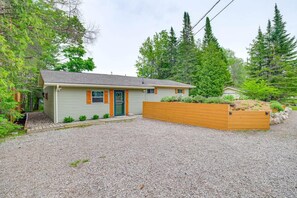 Une maison de plain-pied avec une allée en gravier et un bac à fleurs en bois surélevé devant l’entrée.