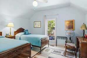 Un dormitorio con dos camas, un escritorio, una silla, un ventanal, un radiador y un ventilador de techo.