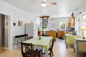 A dining area with a table, chairs, a ceiling fan, and a kitchen in the background.