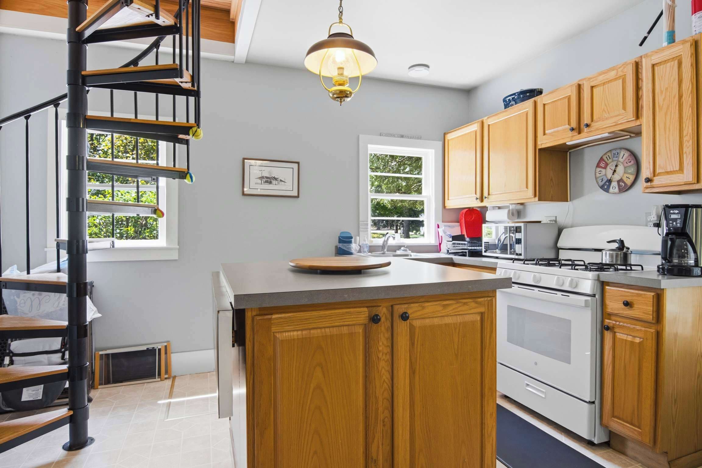 A kitchen with a central island, wooden cabinets, a stove, and a hanging light fixture.