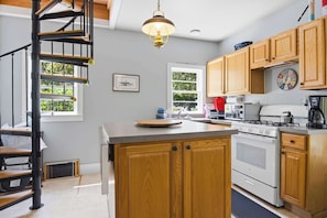 A kitchen with a central island, wooden cabinets, a stove, and a hanging light fixture.