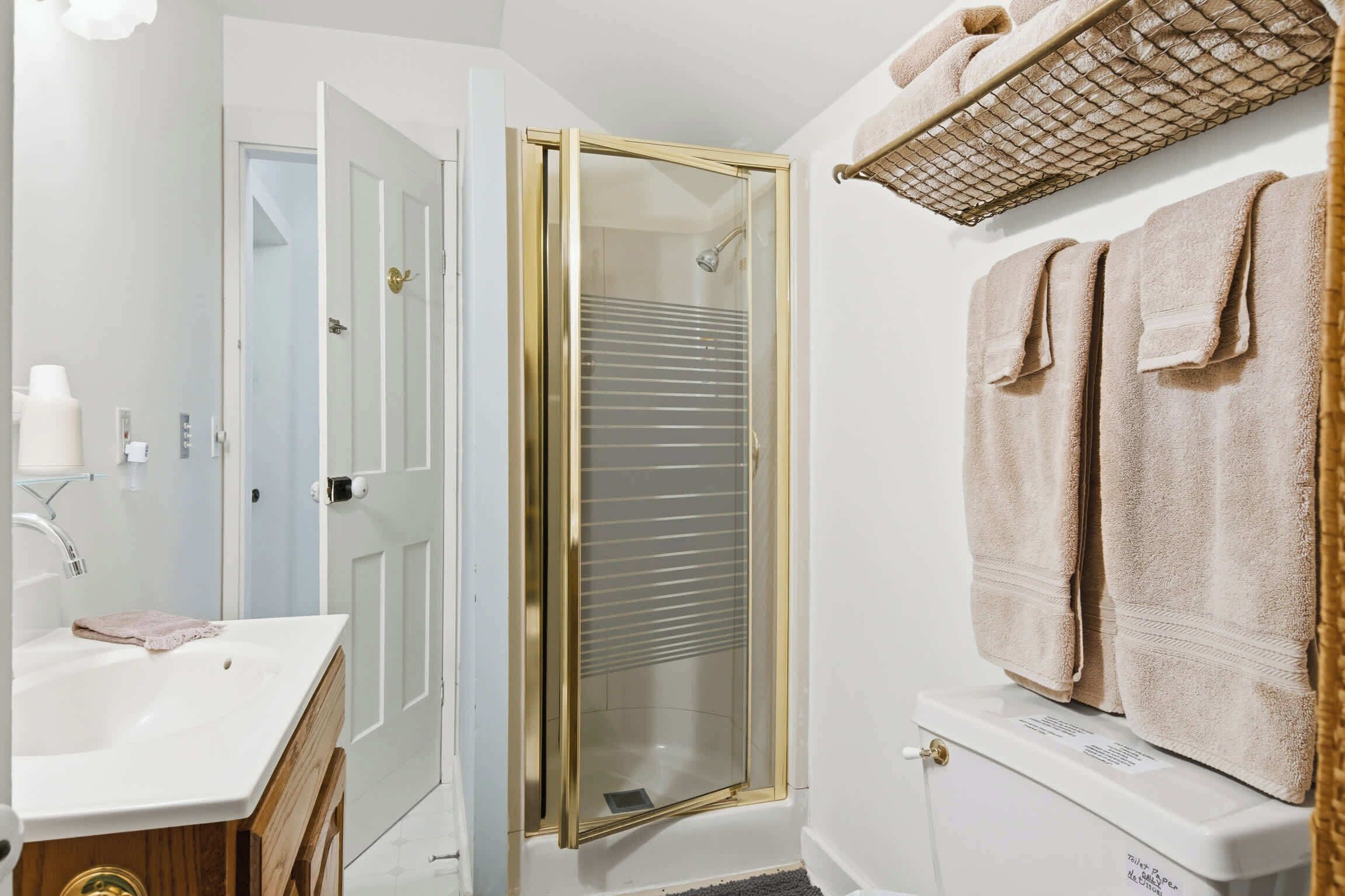 A bathroom with a glass-enclosed shower, a white sink, and a toilet with a towel rack above it.