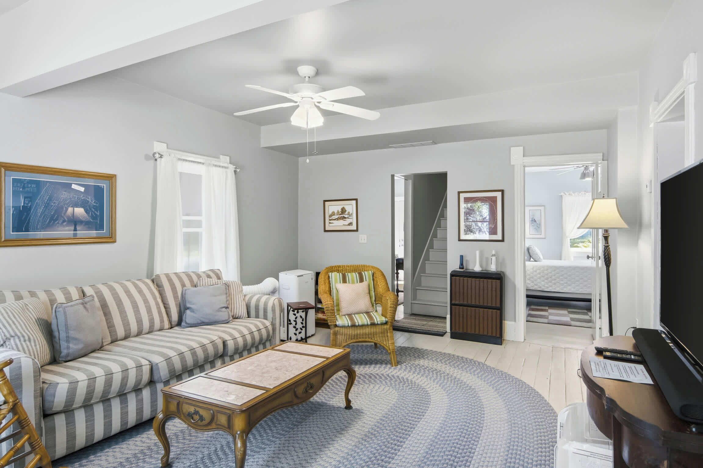 A living room with a striped sofa, a round coffee table, a wicker chair, a ceiling fan, and a television.