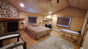 Une chambre confortable dans un chalet, avec une cheminée en pierre, un lit, une chaise, un petit bureau et une salle de bain avec une baignoire.