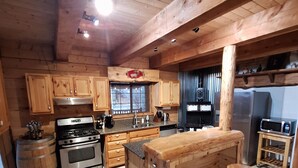 Une cuisine rustique avec des meubles en bois, un îlot central doté de tabourets, une cuisinière et un réfrigérateur.