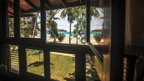 Ein Zimmer mit großen Fenstern und Blick auf einen Strand mit Palmen sowie eine klare Sicht auf den Ozean.