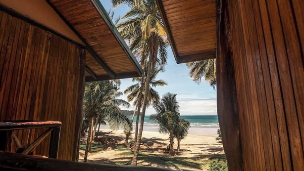Eine Holzhütte mit Blick auf einen Strand und Palmen.
