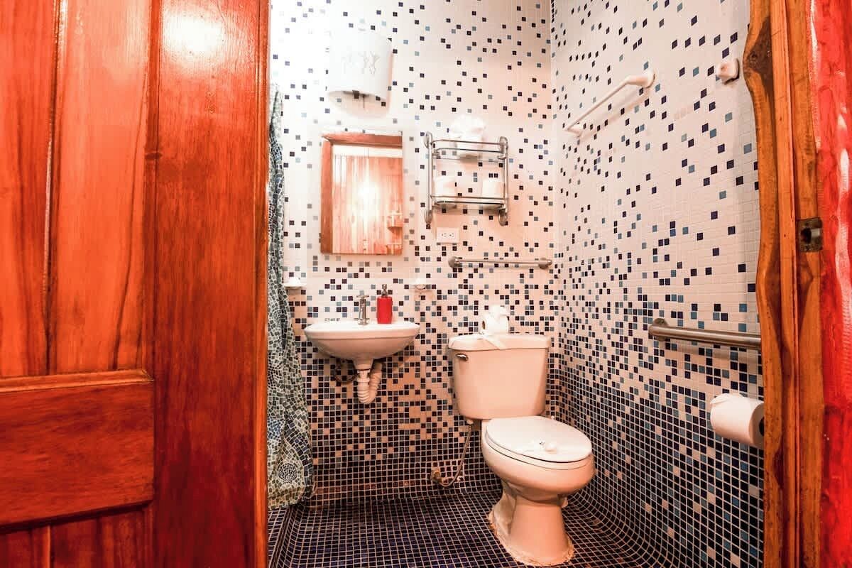 Une salle de bain avec un mur recouvert de mosaïques, une porte en bois, un lavabo et des toilettes.