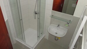 Ein Badezimmer mit einer Duschkabine, einem weißen Waschbecken mit Ablagefläche aus Glas darüber und einem Spiegel an der Wand.