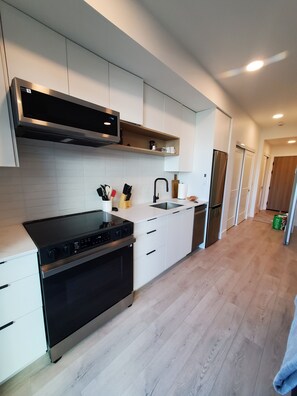 A modern kitchen with white cabinetry, a black stove, and a stainless steel refrigerator. - Kelowna, Sweet Suite Cultural District Pets OK (Kelowna)