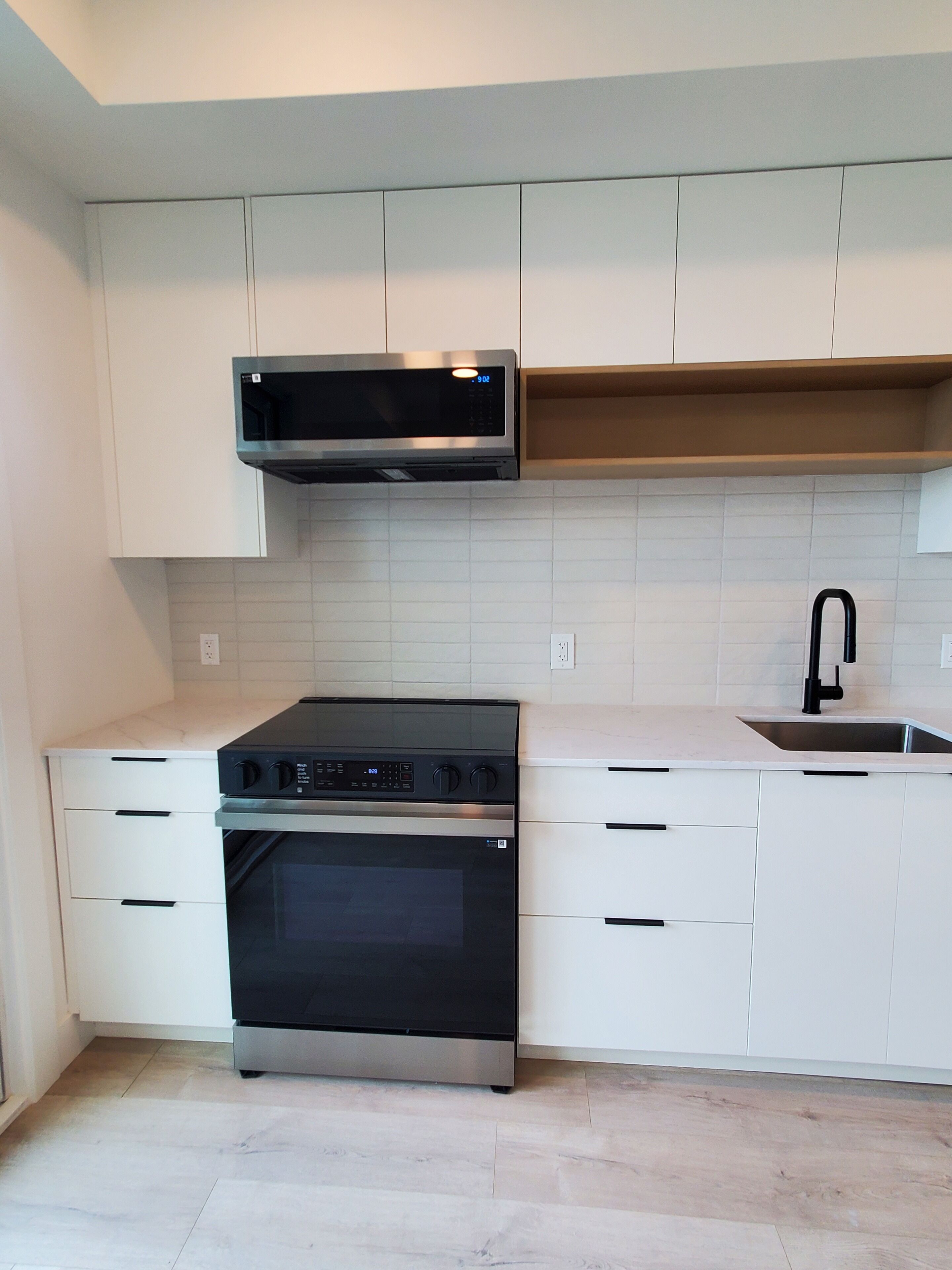 Eine moderne Küche mit weißen Schränken, einer Edelstahl-Mikrowelle, einem eingebauten Backofen und einem Waschbecken mit einem schwarzen Wasserhahn.