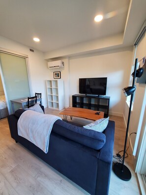 A modern living room with a dark blue sofa, a wooden coffee table, a flat-screen TV, and a black floor lamp. - Kelowna, Sweet Suite Cultural District Pets OK (Kelowna)