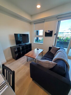 A modern living room with a dark sofa, a wooden coffee table, and a flat-screen TV on a black stand. - Kelowna, Sweet Suite Cultural District Pets OK (Kelowna)