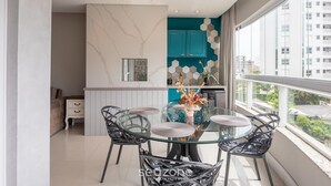 Una cucina moderna con mobili color petrolio, un tavolo da pranzo in vetro e vista sulla città attraverso ampie finestre.