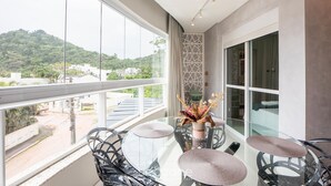 Un balcone con tavolo e sedie in vetro, un vaso decorativo e vista su un pendio verde.