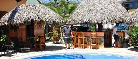 A pool area with thatched umbrellas, wooden furniture, and a bar area.