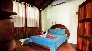 Un dormitorio con una cama de madera, una colcha azul y un cabecero de madera. A la izquierda de la cama hay un banco de madera y a la derecha, una puerta de madera.
