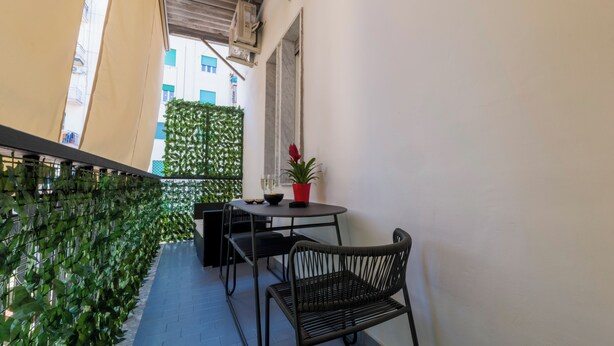 Ein kleiner Balkon mit Tisch und Stühlen, einem Blumentopf und einer grünen Wand.