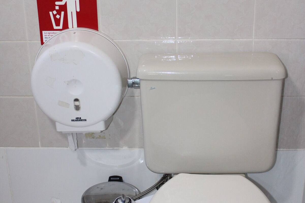 Un inodoro con asiento bidé, un cubo de basura y un letrero rojo de emergencia en la pared.