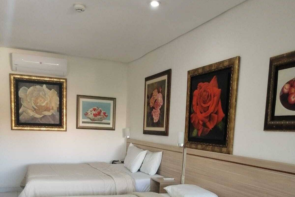 Una habitación de hotel con cuatro camas, un cabecero de madera y tres cuadros enmarcados con motivos florales en la pared.