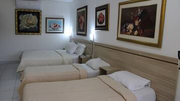 Una habitación de hotel con tres camas individuales, una mesita de noche con lámpara y cuadros en las paredes.