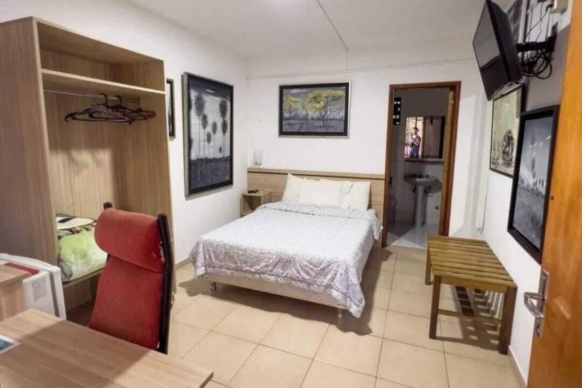 Un dormitorio con cama, escritorio, silla, armario y una mesita.