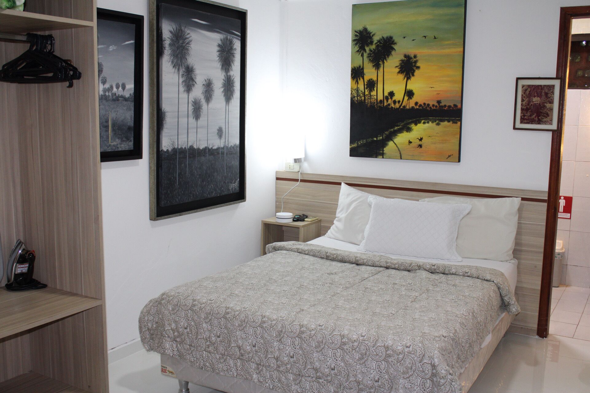 A neatly arranged bedroom with a bed, a nightstand, and a shelf with a hanging item.
