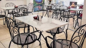 A dining area with metal chairs and tables, artwork on the walls, and a view of the outside. - aparthotel Maison Suisse (Asunción)