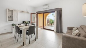 Un salon moderne comprenant un coin repas, un canapé et une vue sur une terrasse extérieure, accessible par une porte vitrée.