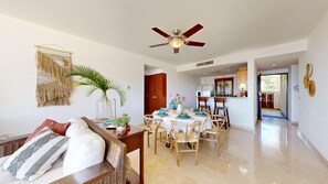 A spacious living area with a dining table set for four, a ceiling fan, and a kitchen in the background.
