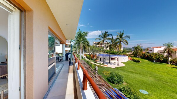 A balcony with a view of a well-maintained lawn, palm trees, and a pool area.