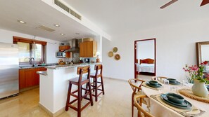 A modern kitchen with wooden cabinets, a built-in microwave, and a granite countertop. There is a dining area with a table set for two, chairs, and a vase with flowers.