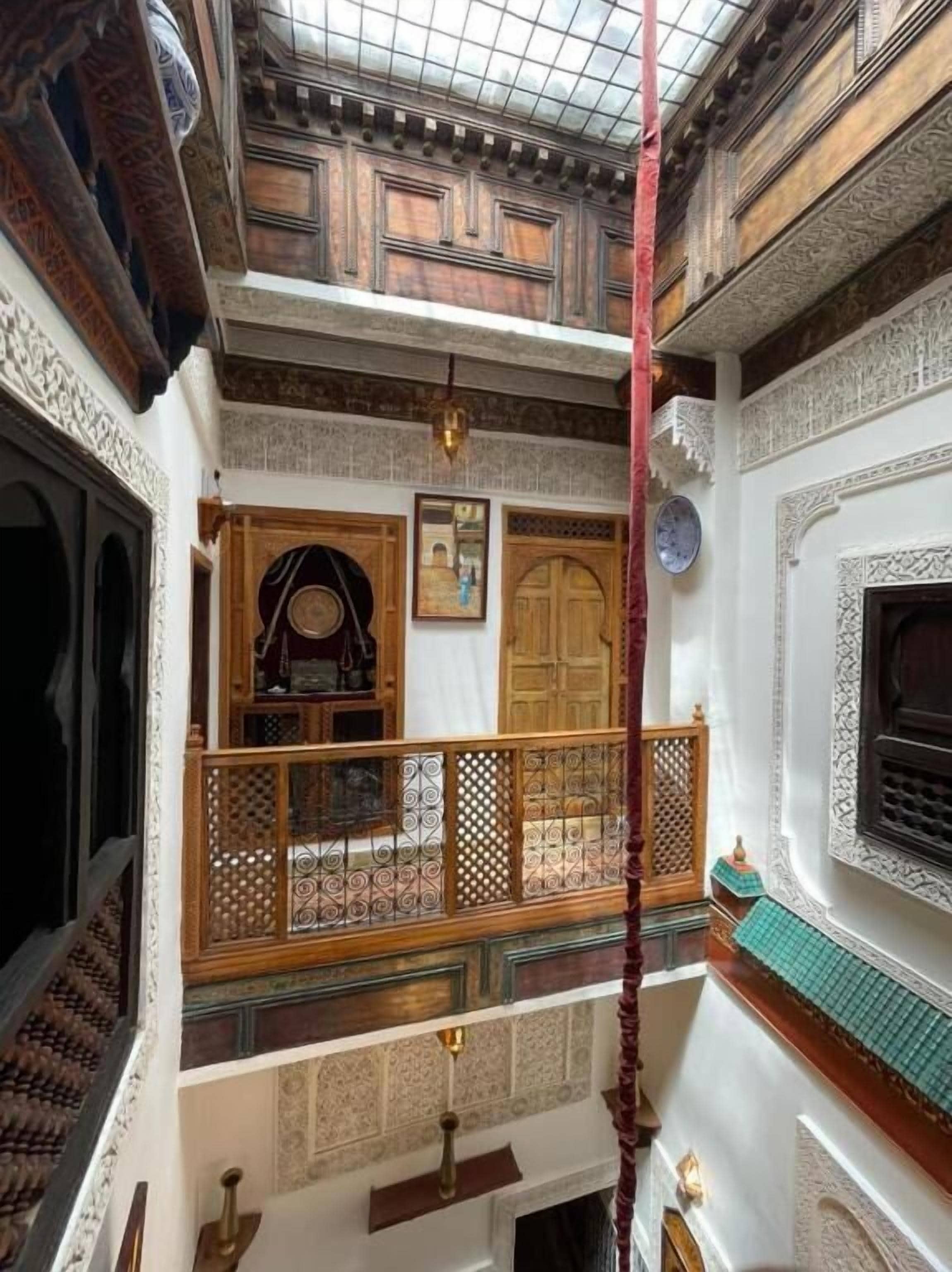Un intérieur traditionnel avec des portes en bois richement décorées, un balcon doté d’une balustrade ornée et un sol carrelé.