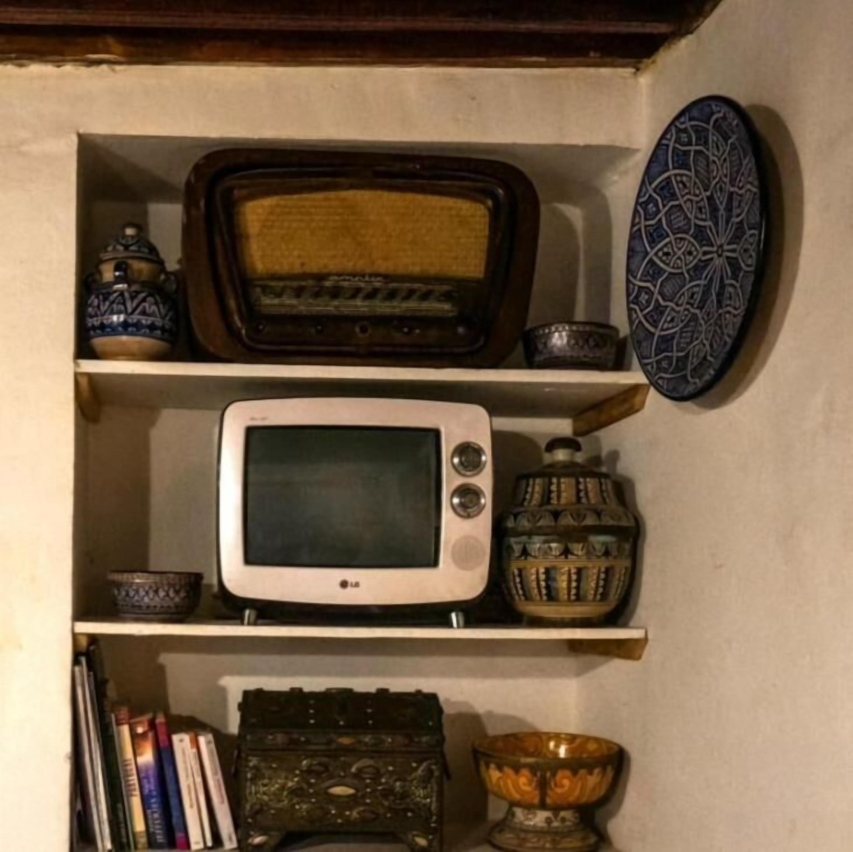 A shelf with a vintage radio, a microwave, decorative bowls, and books.