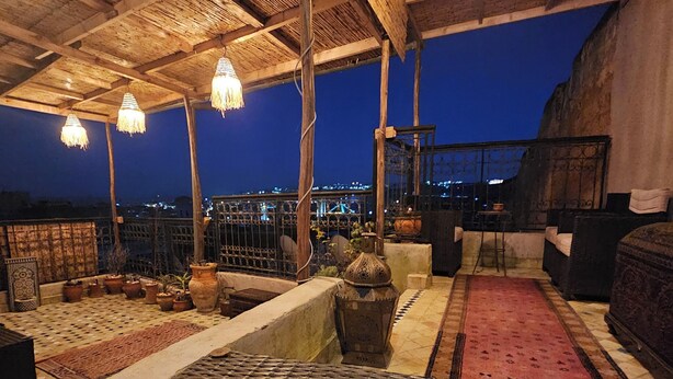A rooftop terrace with a woven table, potted plants, and hanging lights. - Riad Dar Kirami  (Fes)