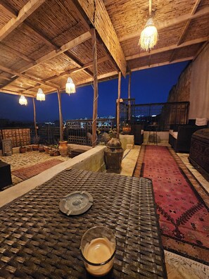 A rooftop terrace with a woven table, potted plants, and hanging lights. - Riad Dar Kirami  (Fes)